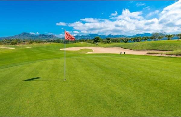 Green golf course with a red flag against mountains and blue sky